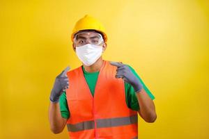 ouvrier du bâtiment asiatique pointant vers son masque de protection et son casque de sécurité photo
