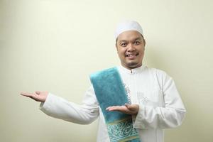 portrait d'un jeune musulman asiatique souriant et pointant vers la présentation de quelque chose de son côté photo