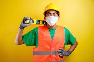homme ouvrier constructeur asiatique avec masque et gilet de sécurité tenir le waterpass sur son épaule photo
