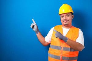 gros travailleur asiatique portant un casque présente quelque chose dans sa main tout en faisant face sur le côté photo