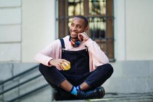 jeune homme noir mangeant une pomme assis sur des marches urbaines. photo