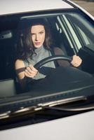 femme brune au volant d'une voiture blanche en milieu urbain photo