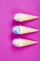 cornes de gaufres à la crème glacée à la vanille avec des oeufs de décoration sur fond rose. minimalisme. concept créatif de pâques. photographie de studio photo