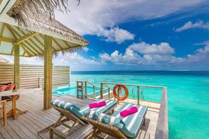 spa luxueux sur pilotis dans le lagon bleu tropical des maldives. incroyable piscine privée, chaise longue en bois, terrasse. vue imprenable sur la mer photo