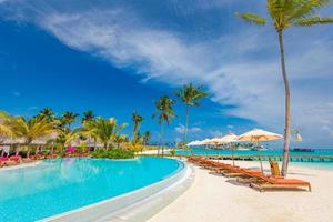 paysage de tourisme de plein air. station balnéaire luxueuse avec piscine et chaises longues ou transats sous des parasols avec palmiers et ciel bleu. concept de fond de voyage et de vacances d'été photo