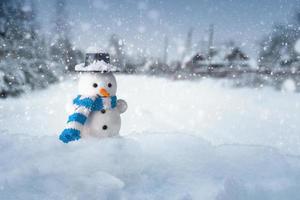 bonhomme de neige se tient dans une congère avec un village en arrière-plan en soirée enneigée photo