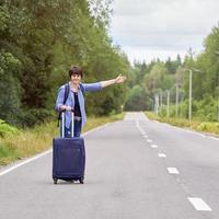 belle femme d'âge moyen avec un sac de voyage faisant de l'auto-stop sur la route rurale en été photo