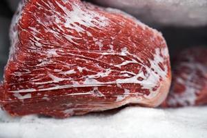 gros morceaux de viande rouge dans un congélateur avec une grande quantité de glace et de neige congelées photo