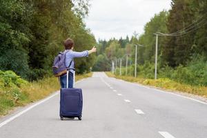 femme d'âge moyen solitaire avec un sac de voyage faisant de l'auto-stop sur la route rurale en été photo