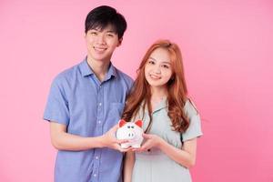 jeune couple asiatique tenant une tirelire sur fond rose photo