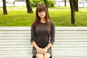 portrait d'une jolie fille avec des lunettes, assise sur un banc dans la rue dans le parc photo