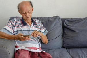 homme âgé asiatique regardant son téléphone sur le canapé bleu de la maison photo