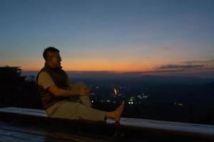 portrait d'homme assis sur une terrasse et regardant le coucher du soleil sur la montagne photo