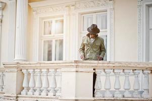 portrait de mode d'un homme afro-américain noir sur un manteau vert et un chapeau noir, restez sur le balcon du manoir jaune photo