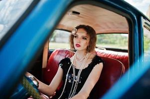 portrait d'un beau modèle de fille de mode bouclée avec un maquillage lumineux dans un style rétro assis sur une voiture d'époque photo