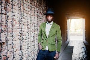 portrait de mode d'un homme afro-américain noir sur une veste en velours vert, un chapeau noir posé au tunnel de la voûte au coucher du soleil photo