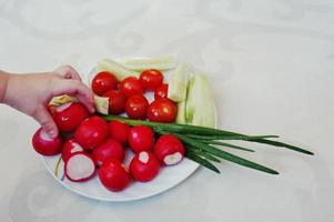 main d'enfant à l'assiette avec des légumes de printemps sur fond de décor blanc photo