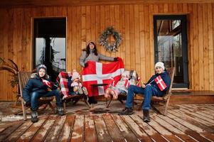 famille avec des drapeaux du danemark près de leur maison en bois. voyage dans les pays scandinaves. les danois les plus heureux. photo