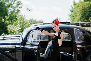 portrait d'une belle mannequin brune sexy avec un maquillage lumineux dans un style rétro près d'une voiture vintage avec une cigarette à la main. photo