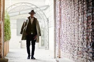 portrait de mode d'un homme afro-américain noir sur une veste en velours vert, un chapeau noir et un manteau sur ses épaules posés au tunnel de la voûte photo