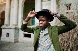 portrait de mode en gros plan d'un homme afro-américain noir sur une veste en velours vert et un chapeau noir, arrière-plan vieille maison vintage avec arche et colonnes photo