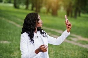 portrait en gros plan d'une élégante fille afro-américaine noire prenant un selfie avec un téléphone mobile rose photo