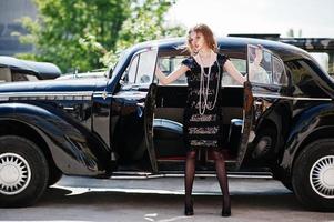 portrait de beau modèle de fille de mode bouclée sexy avec un maquillage lumineux dans un style rétro près d'une voiture vintage photo