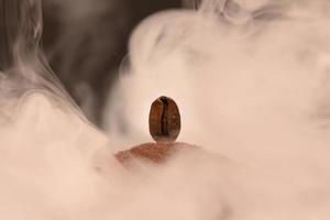 un grain de café fraîchement torréfié repose sur une dispersion de café moulu dans la fumée. photo