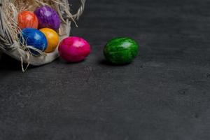 oeufs de pâques peints multicolores dans un panier sur fond de pierre sombre. photo