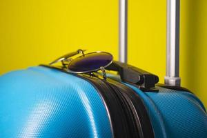 valise bleue avec lunettes de soleil sur fond jaune. notion de voyage.