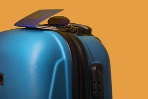 valise bleue avec lunettes et passeport sur fond orange.