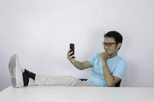 jeune homme asiatique choqué quand il regarde un smartphone avec une jambe sur la table photo