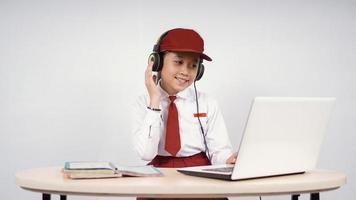 Fille asiatique de l'école primaire à l'écoute au casque tout en étudiant isolé sur fond blanc photo