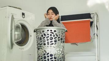 femme asiatique en hijab qui est sale en regardant des tas de vêtements sales à la maison photo