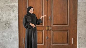 femme en robe musulmane noire pointant d'un air absent vers le côté devant la porte photo