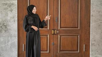 femme en robe musulmane noire pointant d'un air absent vers le côté devant la porte photo