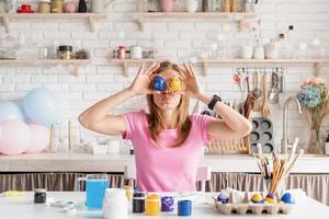 femme colorant des oeufs de pâques dans la cuisine, tenant des oeufs à côté des yeux photo