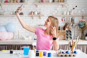 femme colorant des oeufs de pâques dans la cuisine, prenant selfie photo