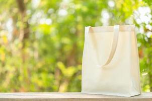 sac en coton blanc posé sur une table en bois avec un espace pour le texte ou la publicité. le sac en coton peut être utilisé pour faire du shopping pour remplacer le sac en plastique sur la nature verte photo