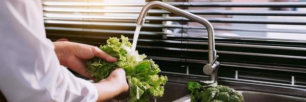 mains asiatiques femme lavant la salade de légumes et préparant des aliments sains dans la cuisine. photo