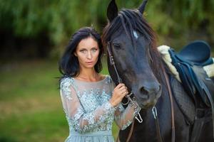 Belle femme en robe avec cheval noir dans la nature photo