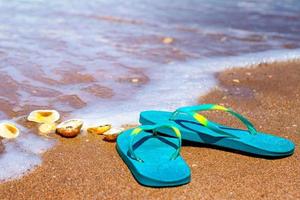 des pantoufles bleues se tiennent sur le sable au bord de la mer photo