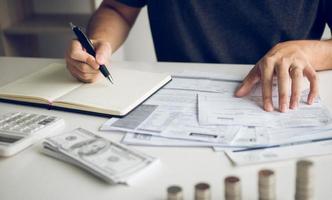 l'homme utilise des calculatrices et des documents qui calculent les dépenses au bureau à domicile. photo