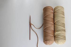 crochet beige et un écheveau de cordon beige sur fond blanc. sur un crochet - une boucle du cordon, faite pour commencer à tricoter. un tel cordon peut faire un tapis, un accessoire, etc. photo