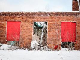 ancien bâtiment en brique rouge avec porte cassée, fenêtres rouges fermées et toit et sol couverts de neige photo