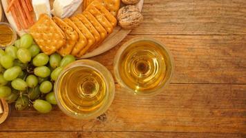 raisins verts, craquelins, noix et deux verres de vin blanc sur fond de bois photo