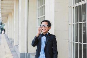 mignon garçon asiatique portant un costume noir vintage et des lunettes parler au téléphone en souriant photo