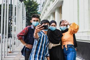 amis avec masque de protection s'amusant à prendre des selfies pendant la pandémie de coronavirus en été. photo