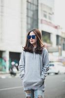 jolie femme asiatique portant un sweat à capuche gris et des lunettes de soleil posant dans la rue de la ville photo