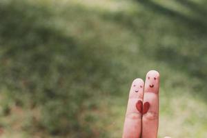 forme de coeur rouge sur deux doigts avec image de visage tout en souriant visage avec fond bokeh nature. espace de copie. heureux couple amoureux. photo